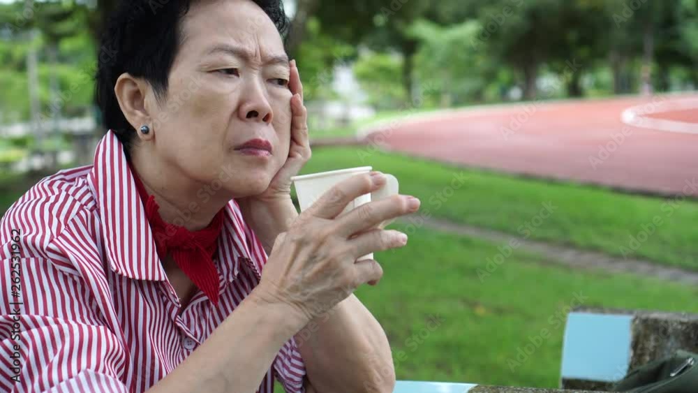 Asian senior woman worry thinking in park drinking coffee Asian senior woman worry thinking in park drinking coffee