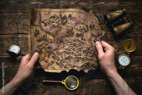 Vászonkép Old map in man adventurer hands on a brown table background