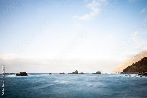 Sea view, marine panorama of the coast at sunset, sea, mountains, rocks, clouds and waves with soft light. Tenerife island coast and sea at sunset