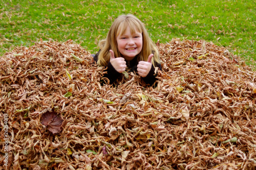 Young girl in fall leaves with thumbs up