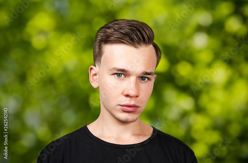 portrait white young guy model dressed in black t-shirt looking at the camera on green bokeh background