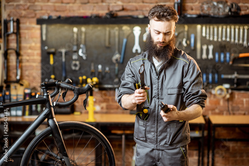 Portrait of a handsome bearded repairman in workwear standing with wrenches at the bicycle workshop © rh2010