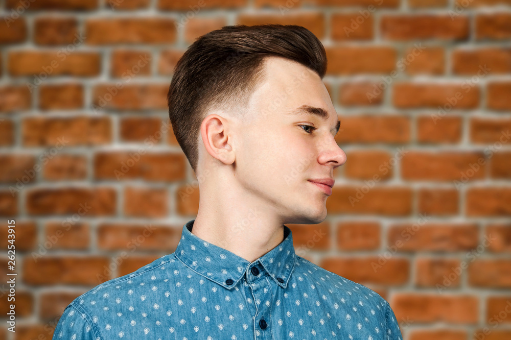 White young guy dressed in blue shirt on brick wall background smiles and looking aside White young guy dressed in blue shirt on brick wall background smiles and looking aside