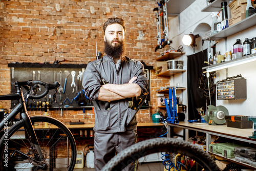 Portrait of a handsome bearded repairman in workwear standing with wrenches at the bicycle workshop © rh2010