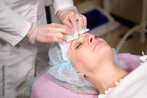 Cosmetologist remove a face mask to her patient . Anti-ageing and smoothing procedure in a beauty salon. Doctor in a cosmetological clinic making a treatment of skin care
