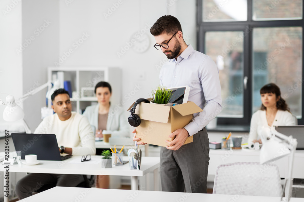 business, firing and job loss concept - fired male office worker with box of his personal stuff and his sad colleagues