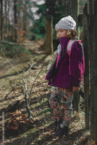Portrait of a little caucasian girl in a forest. Child dressed in a jacket and hat  large blur background.