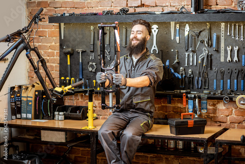 Portrait of a handsome repairman in workwear sitting with bicycle fork on the table in the bicycle workshop