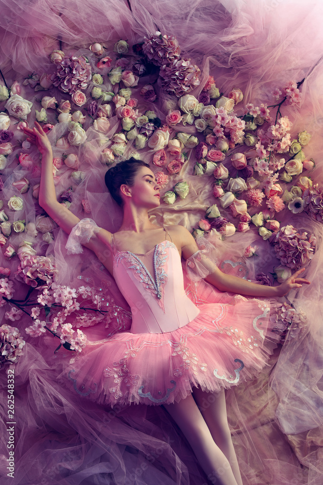 Beauty of sadness. Top view of beautiful young woman in pink ballet tutu surrounded by flowers. Spring mood and tenderness in coral light. Art photo. Concept of spring, blossom and nature's awakening.