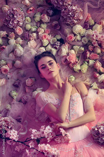 Delicacy. Top view of beautiful young woman in pink ballet tutu surrounded by flowers. Spring mood and tenderness in coral light. Art photo. Concept of spring, blossom and nature's awakening. photo