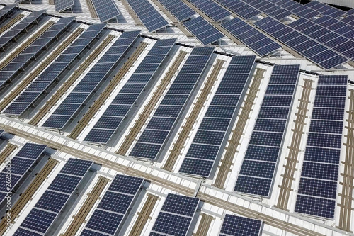 Solar panels spread across an industrial roof - Aerial image.