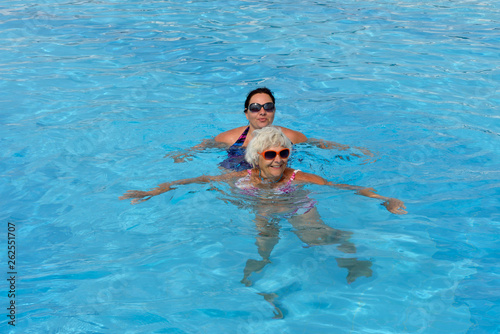 Two women are swimming in bright blue water of pool.