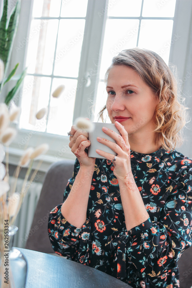 Beautiful romantic young blonde woman in dress with cup of tea sitting by the window. Feminine jewelry, mehendi Beautiful romantic young blonde woman in dress with cup of tea sitting by the window. Feminine jewelry, mehendi