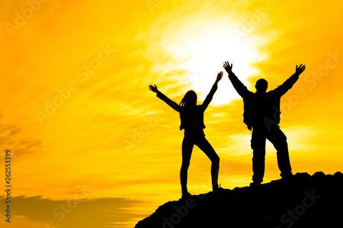Two people between clouds Full length silhouette of happy couple stand together on peak of a mountain with hands raised up, sunset and ocean. Man and woman on top mountain look at beautiful night