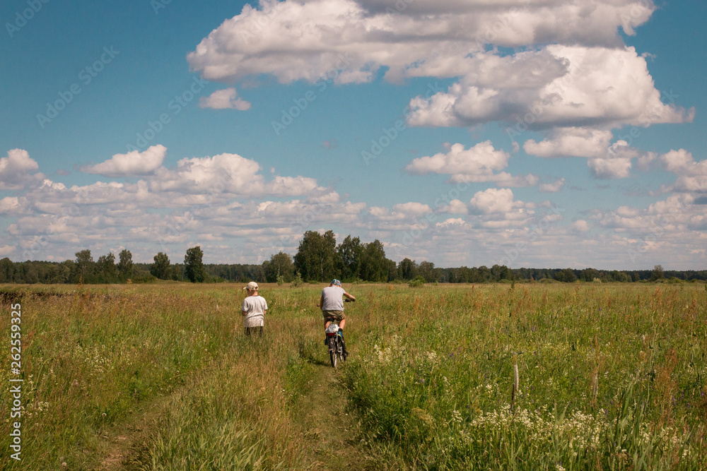 Children walk in a field of green grass. Bright blue sky with white clouds. Boys travel on a bright summer day. Landscape. Children walk in a field of green grass. Bright blue sky with white clouds. Boys travel on a bright summer day. Landscape.
