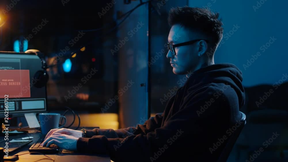 cybercrime, hacking and technology concept - asian male hacker writing code or using computer virus program for cyber attack and drinking coffee in dark room at night cybercrime, hacking and technology concept - asian male hacker writing code or using computer virus program for cyber attack and drinking coffee in dark room at night