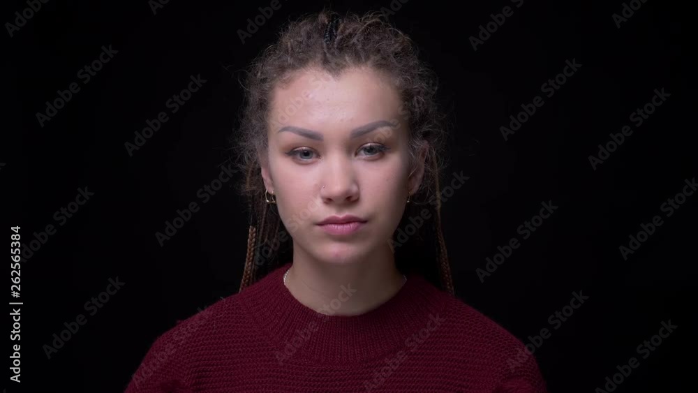Eccentric and cool brunette girl with dreadlocks watching frostily into camera on black background. Eccentric and cool brunette girl with dreadlocks watching frostily into camera on black background.