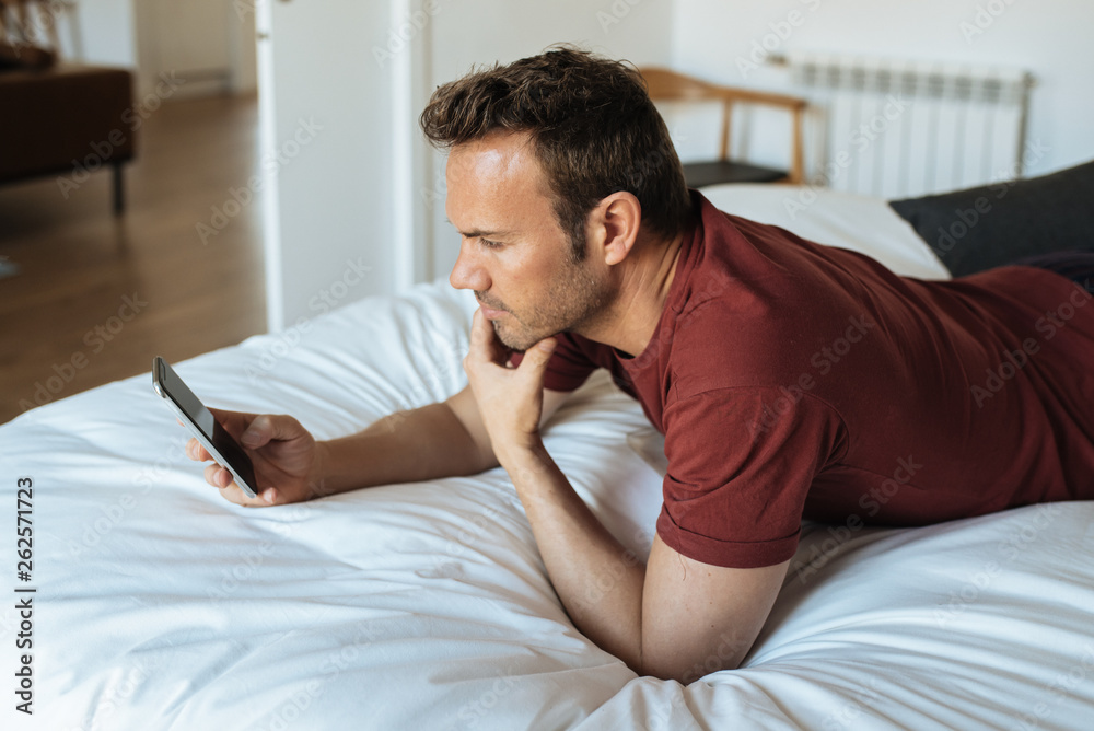 Man lying down on bed with mobile phone Man lying down on bed with mobile phone