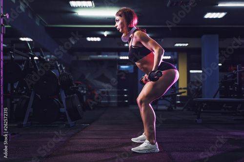 Attractive fit sexy woman in the gym crouches with a barbell. Woman training back. Colored smoke