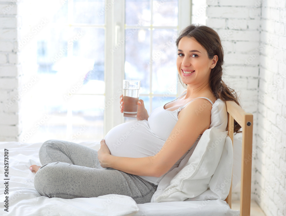 portrait of a pregnant dark-haired girl on the bed with a glass of water portrait of a pregnant dark-haired girl on the bed with a glass of water