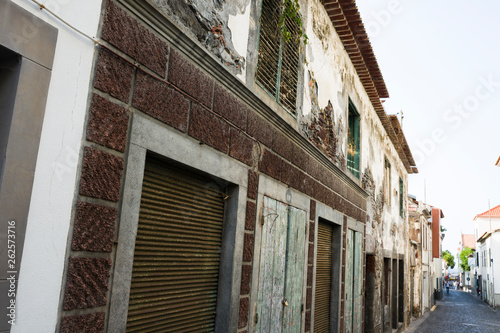 Narrow European street. In the foreground is a two-storey old house, in the background are other houses and rare pedestrians.