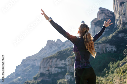 Trail runner with open arms raised while enjoying nature on mountain peak.