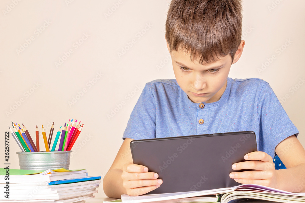 Kid sitting at table with books notebooks and using tablet computer Kid sitting at table with books notebooks and using tablet computer