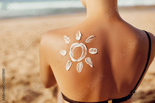 Skin care. Sun protection. Woman apply sun cream. Woman With Suntan Lotion On Beach In Form Of The Sun. Portrait Of Female With  Drawn Sun On A Shoulder. Suncream. Girl Holding Moisturizing Sunblock.