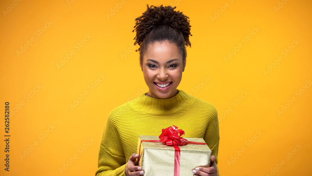 Young woman smiling on camera holding present in hands, holiday celebration Young woman smiling on camera holding present in hands, holiday celebration