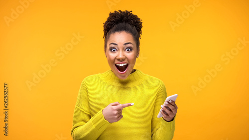 Joyful young woman pointing at smartphone in hand, online shopping application photo