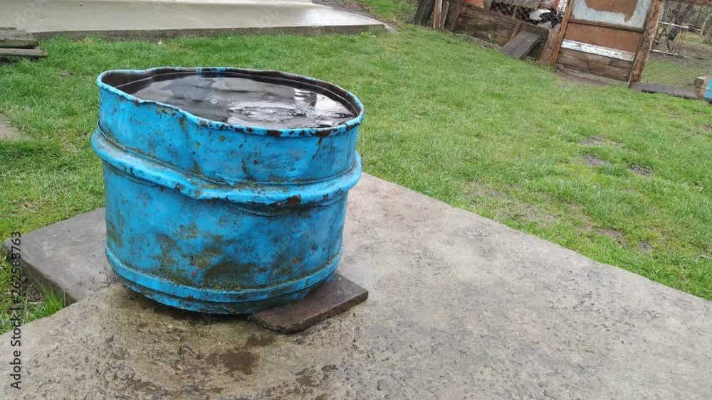 rain water flowing into an old rusty barrel far away view rain water flowing into an old rusty barrel far away view