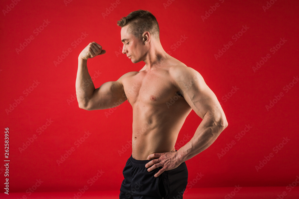 handsome young man in athletic form on red background shows his muscles