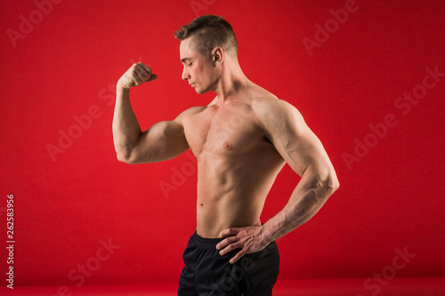 handsome young man in athletic form on red background shows his muscles © Alexandr