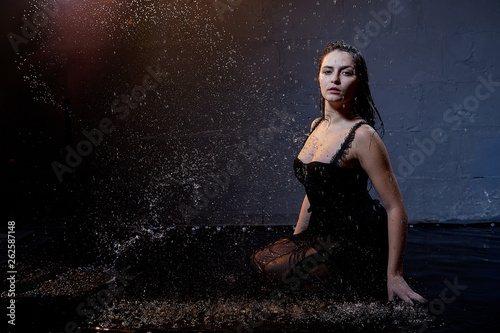 Beautiful sexy girl in black and water spray in the Studio on a dark background with orange back light