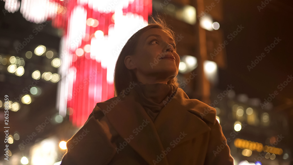 Female tourist standing on brightly illuminated street, enjoying festive lights