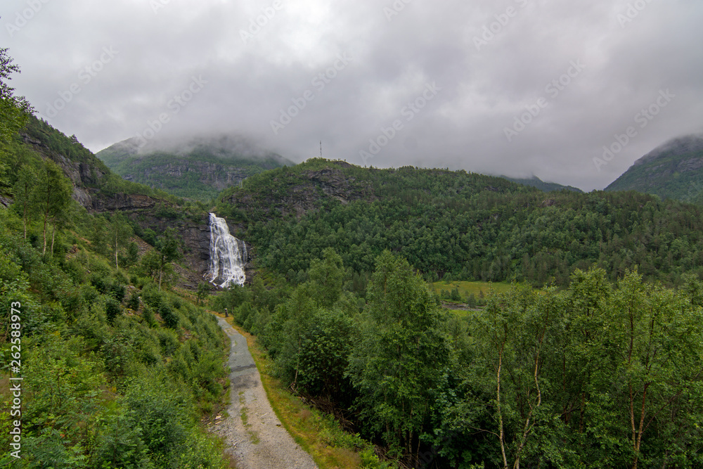 Fototapeta premium Wasserfall mit schmaler Straße in den Bergen