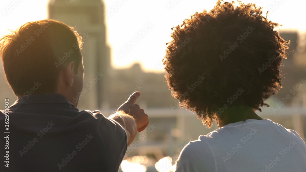 Beautiful multiracial couple looking at city from the roof at sunny day, date