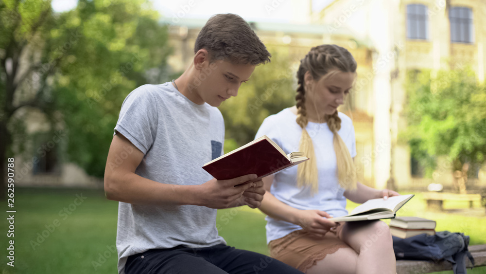 Two teenagers reading books in park, preparing for examination, studying Two teenagers reading books in park, preparing for examination, studying
