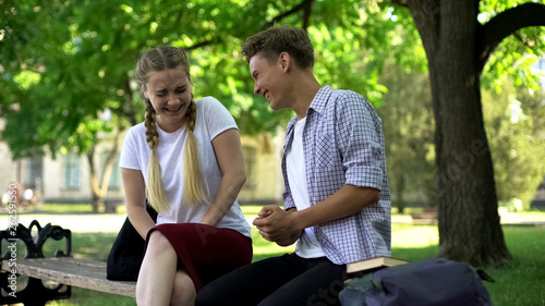 Laughing friends sitting on bench in park, telling extremely funny story, joke © motortion