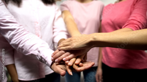 Group of women in pink shirts putting hands together, gender equality, feminism