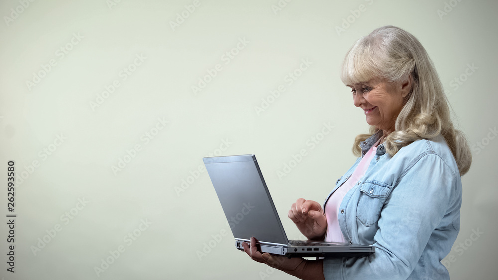 Happy elderly female typing on laptop, communicating with children, technologies Happy elderly female typing on laptop, communicating with children, technologies