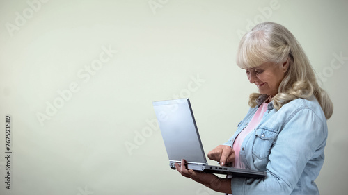 Old woman typing on laptop, looking for goods and shopping, modern technologies