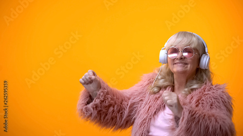 Positive elderly lady in pink coat and round sunglasses listening to music