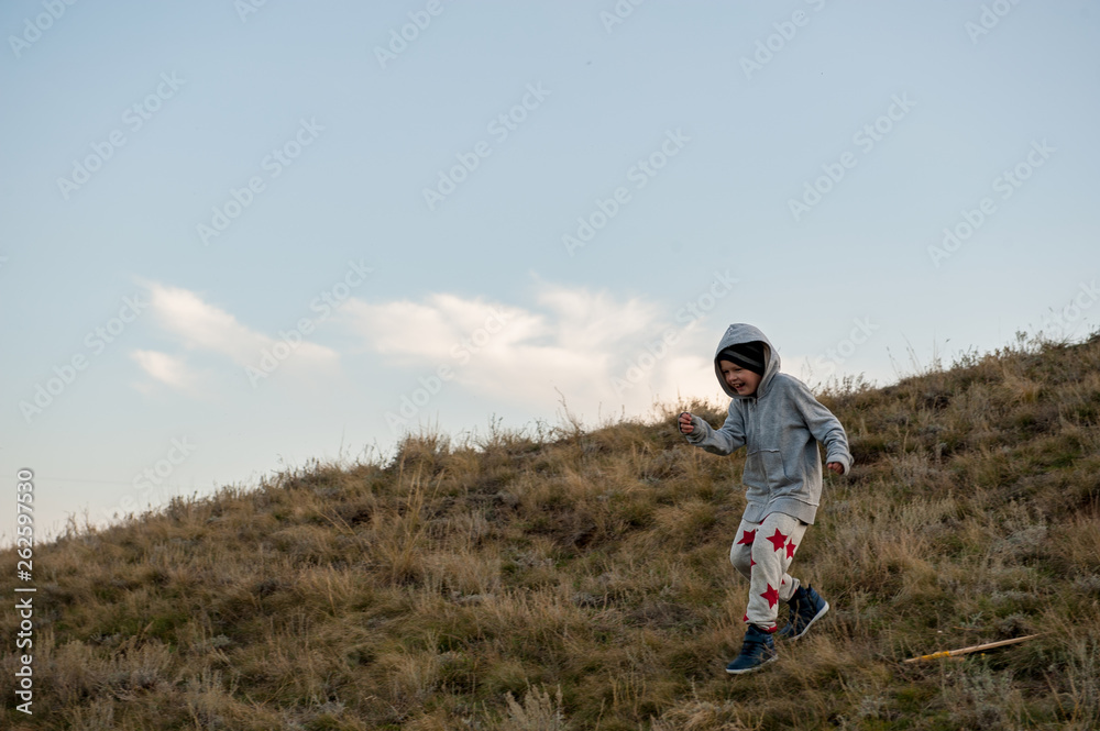 Upset child playing in field sown with winter wheat against backdrop of rain clouds. Tradition of respect for nature, sports and harmonious life.