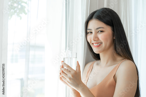 Beautiful beauty woman Asian cute girl feel happy drinking Clean drink water for good health in the morning , enjoying time in her home white bedroom background - lifestyle beauty woman concept
