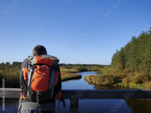 man with orange backpack on the wood bridge. hiker is watching the river and the forest
