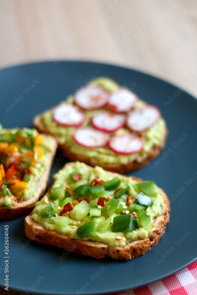 Three slices of toast with mashed avocado and various vegetable and herb toppings. Selective focus. Three slices of toast with mashed avocado and various vegetable and herb toppings. Selective focus.