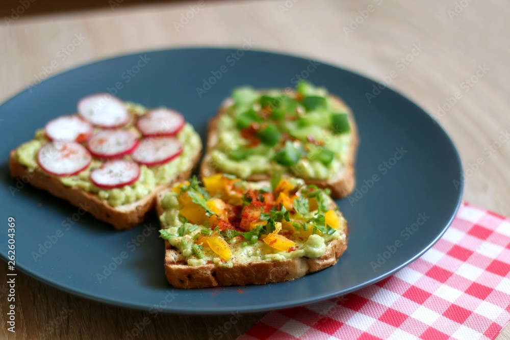 Three slices of toast with mashed avocado and various vegetable and herb toppings. Selective focus. Three slices of toast with mashed avocado and various vegetable and herb toppings. Selective focus.