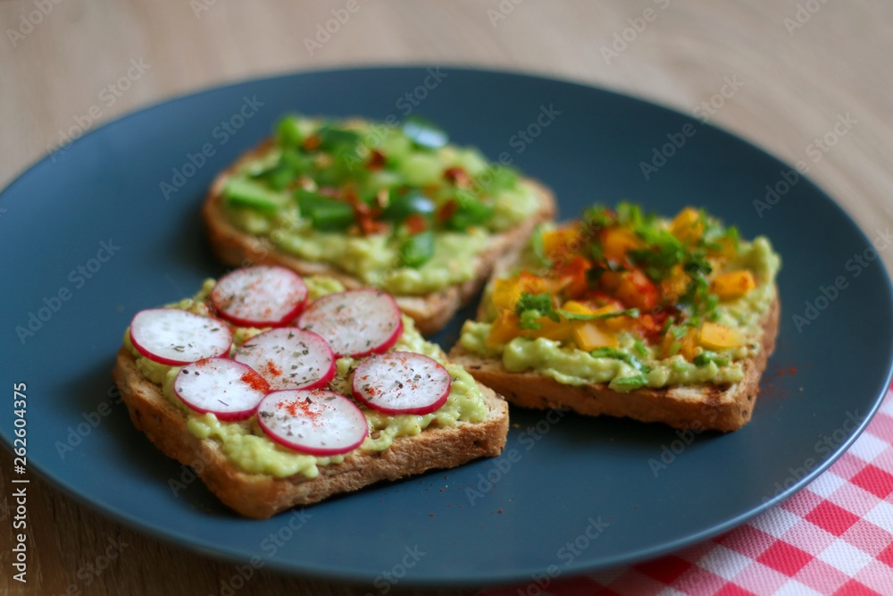 Three slices of toast with mashed avocado and various vegetable and herb toppings. Selective focus. Three slices of toast with mashed avocado and various vegetable and herb toppings. Selective focus.
