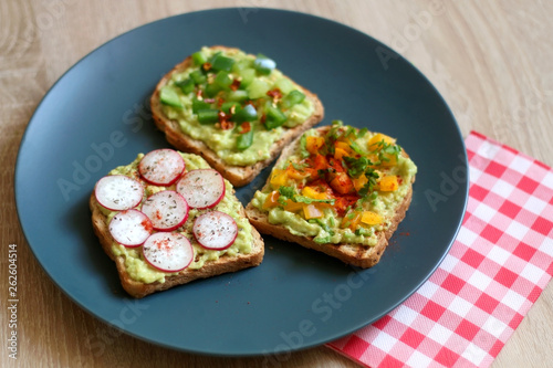 Three slices of toast with mashed avocado and various vegetable and herb toppings. Selective focus.